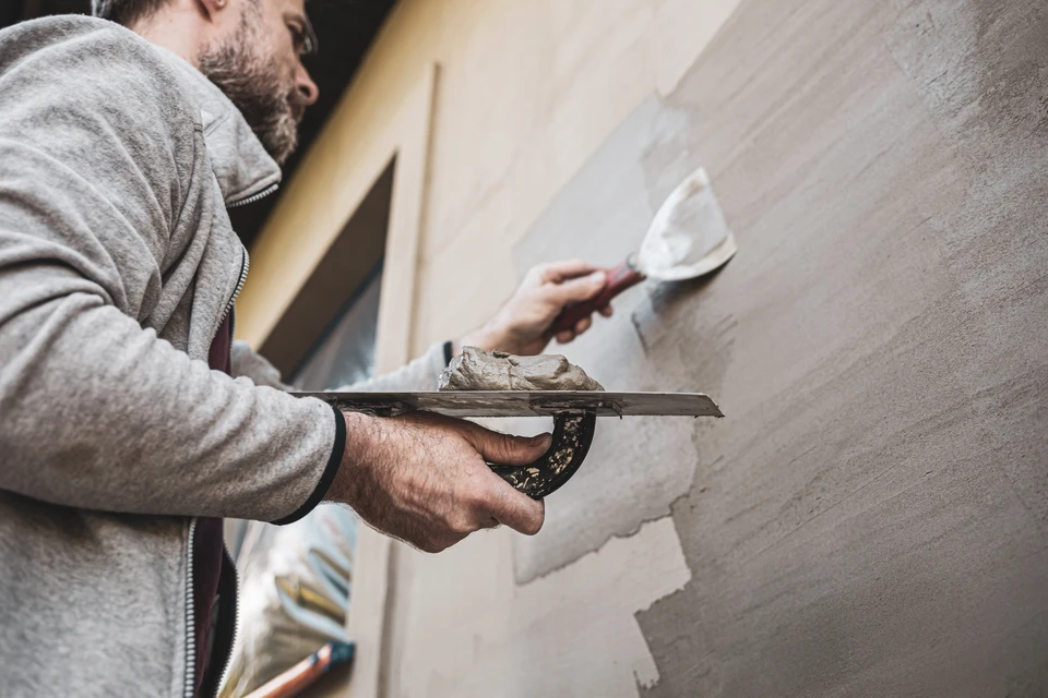 Artisan plâtrier en tenue de travail applique un enduit sur mur intérieur avec taloche