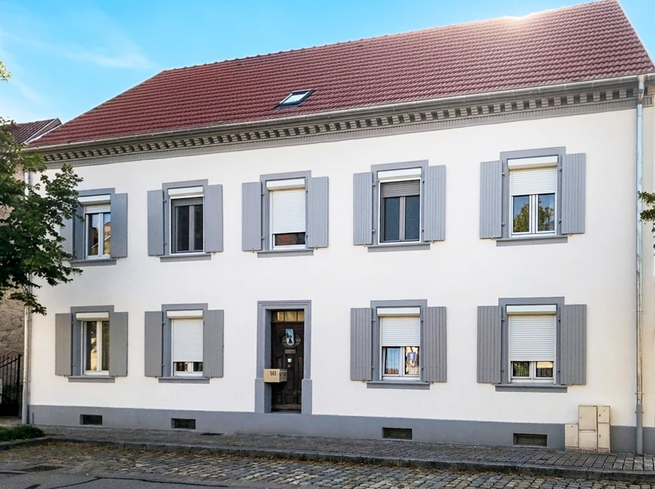 Photographie d'un détail en gros plan montrant la texture et la finition d'une façade récemment peinte, avec les coups de rouleau visibles et le contraste entre la surface peinte neuve et l'ancienne façade adjacent, illustrant le résultat de qualité du travail de peinture extérieure. L'image doit montrer les détails techniques du rendu final, mettant en évidence la finition professionnelle obtenue.