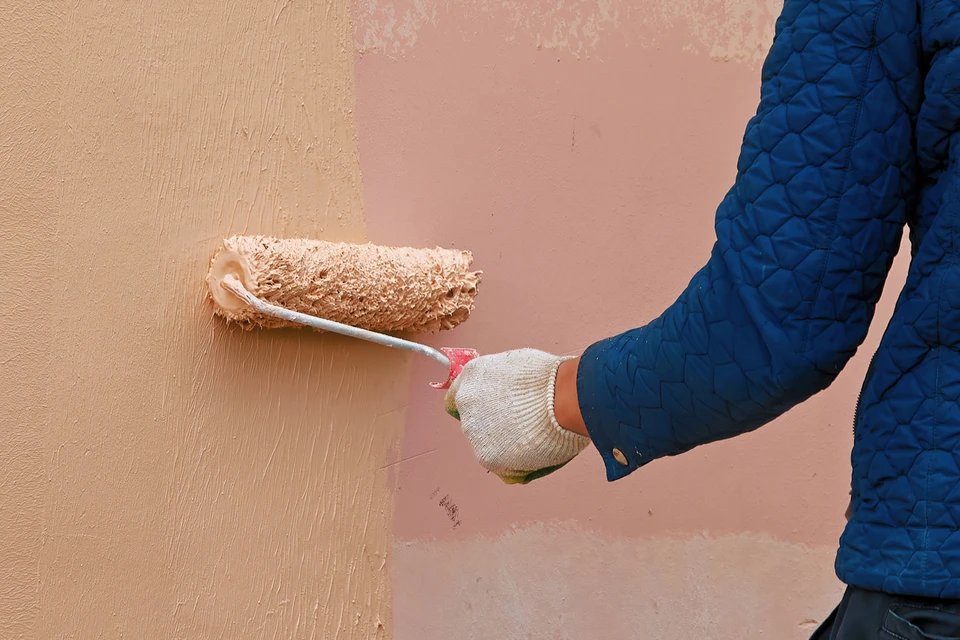 Ouvrier en équipement de protection individuelle appliquant de la peinture sur façade extérieure d'immeuble