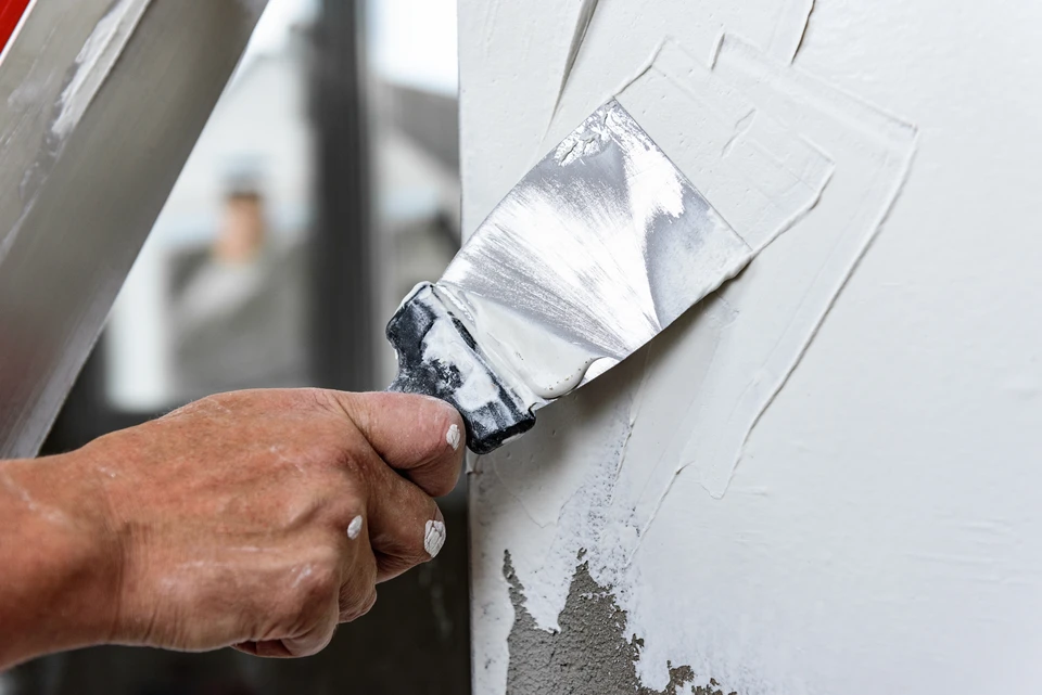 Un ouvrier portant un chapeau bleu dur et des gants de sécurité place soigneusement un matériau d'isolation contre un mur