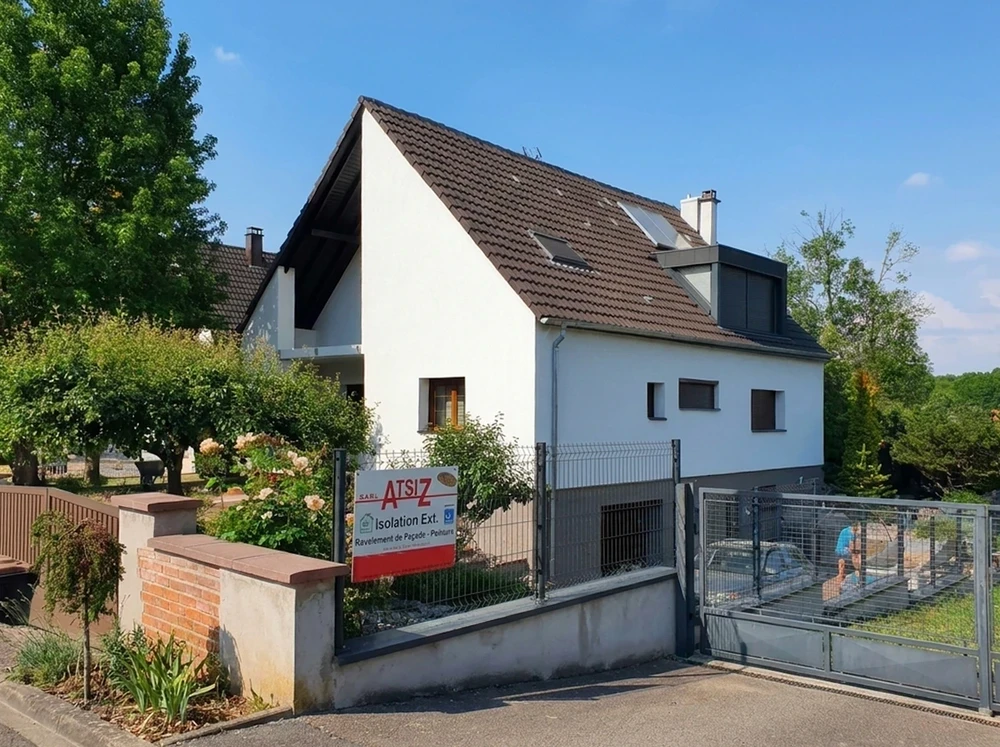 Façade d'une maison individuelle rénovée, enduit blanc lisse, toiture en tuiles plates brun foncé avec fenêtres de toit Velux